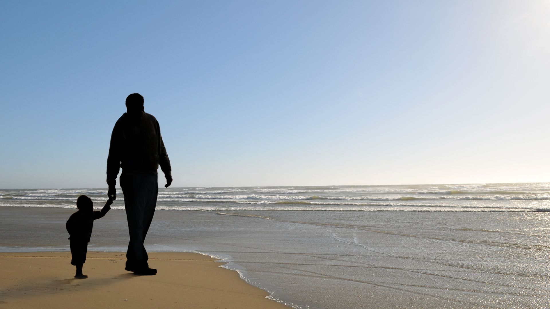A peaceful scene of a father walking on the beach with his young son, holding hands. 