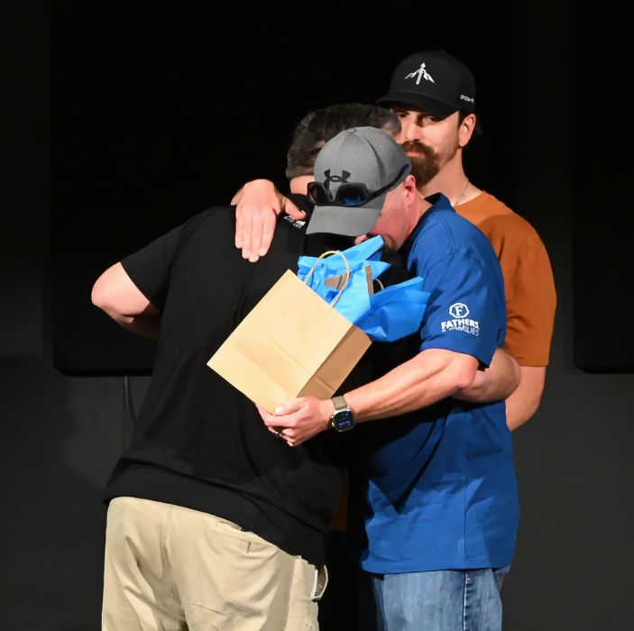 Two men hugging on stage at a ManAlive event