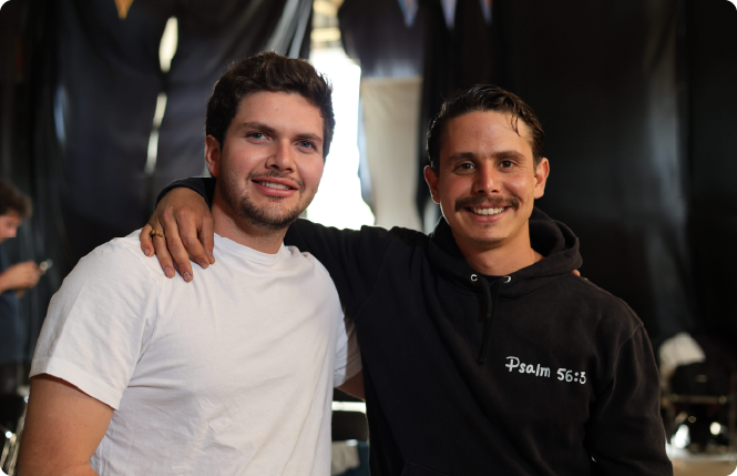 Man with gray hair and beard in navy suit and tie sitting with hands clasped, looking thoughtful.