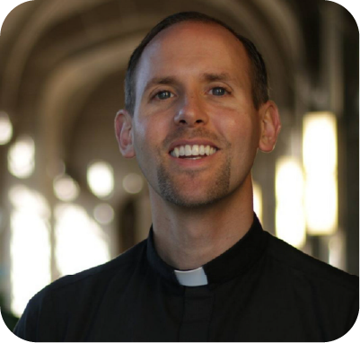 Man with dark hair and beard wearing a white shirt and blue blazer against a light background.