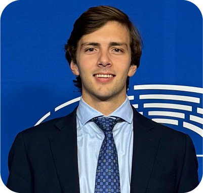 Man with dark hair and beard wearing a white shirt and blue blazer against a light background.