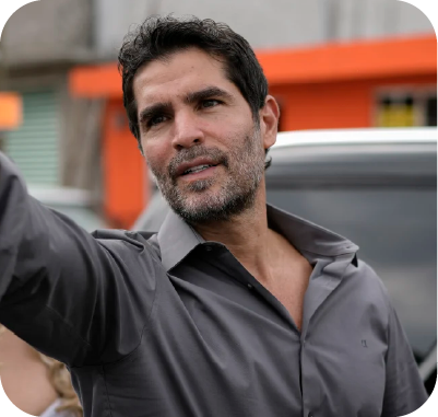 Two men smiling on stage with colorful floral jackets, one holding a microphone.