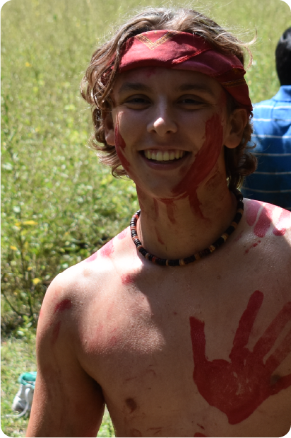 Man with grey beard and curly hair dressed in a dark suit and tie, sitting with fingers interlaced in front of a dark background.