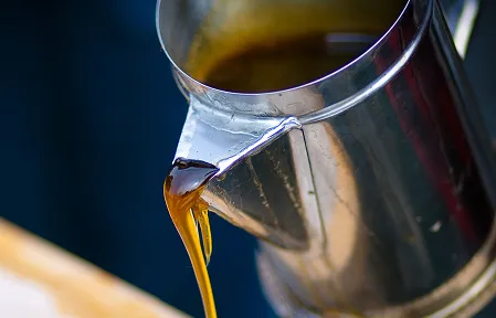 Fresh-made maple syrup, a staple in the Northeast Region, is being poured out of a silver pitcher.
