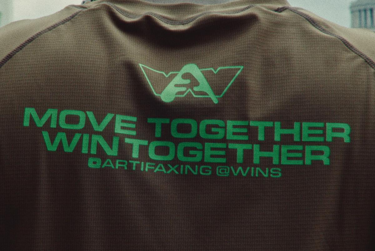  Close-up of the back of an Active Tee featuring a neon green logo above bold text that reads “MOVE TOGETHER, WIN TOGETHER,” with smaller text showing “@ARTIFAXING @WINS.”