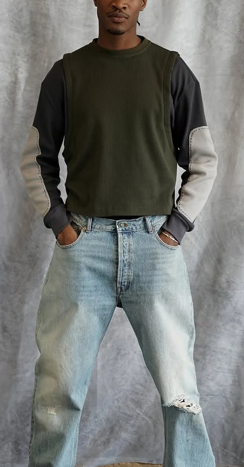 Model in Todd Patrick color-block long-sleeve and light-wash relaxed jeans with knee rip, standing against a gray studio backdrop.