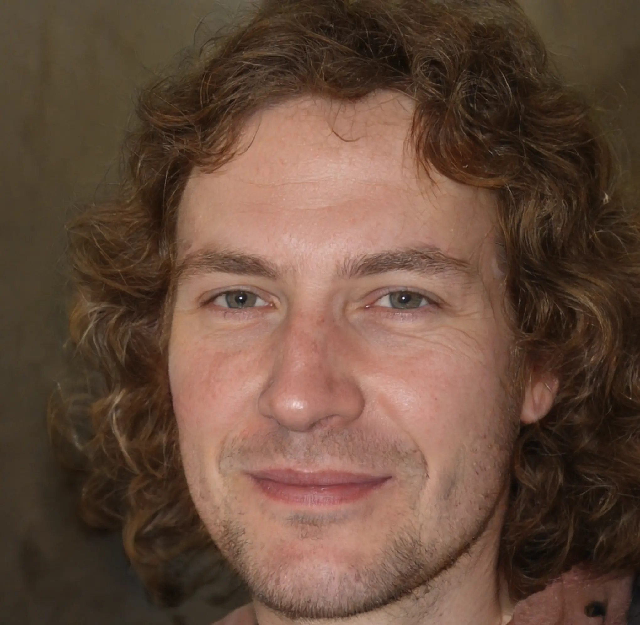 Close-up of a man with curly light brown hair and blue eyes smiling gently.