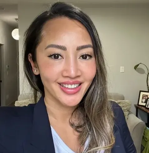 Smiling woman with long dark hair wearing a navy blazer and light blue shirt in a living room.