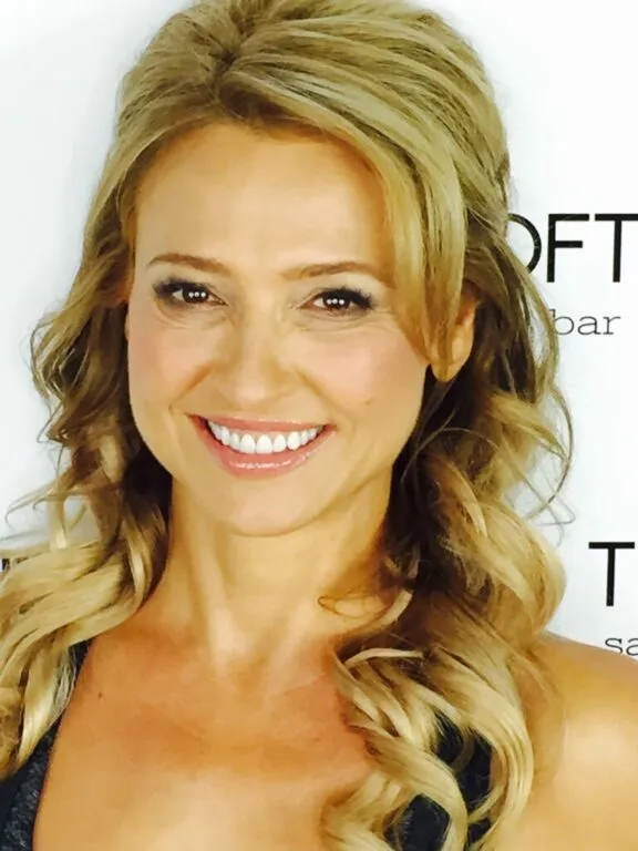 Smiling woman with long wavy blonde hair wearing a black top against a white background with text.
