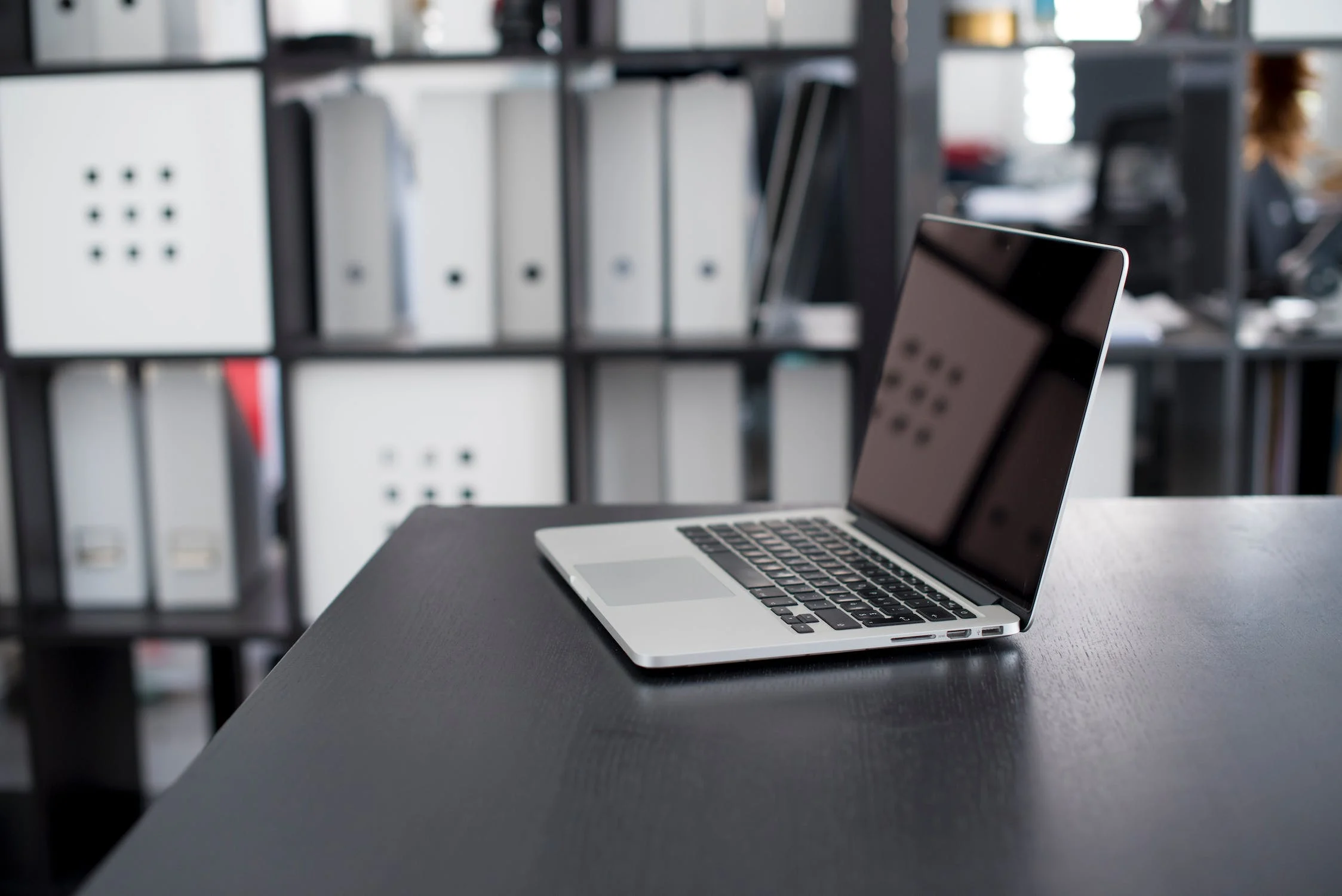 Laptop on an office desk in front of shelves of binders