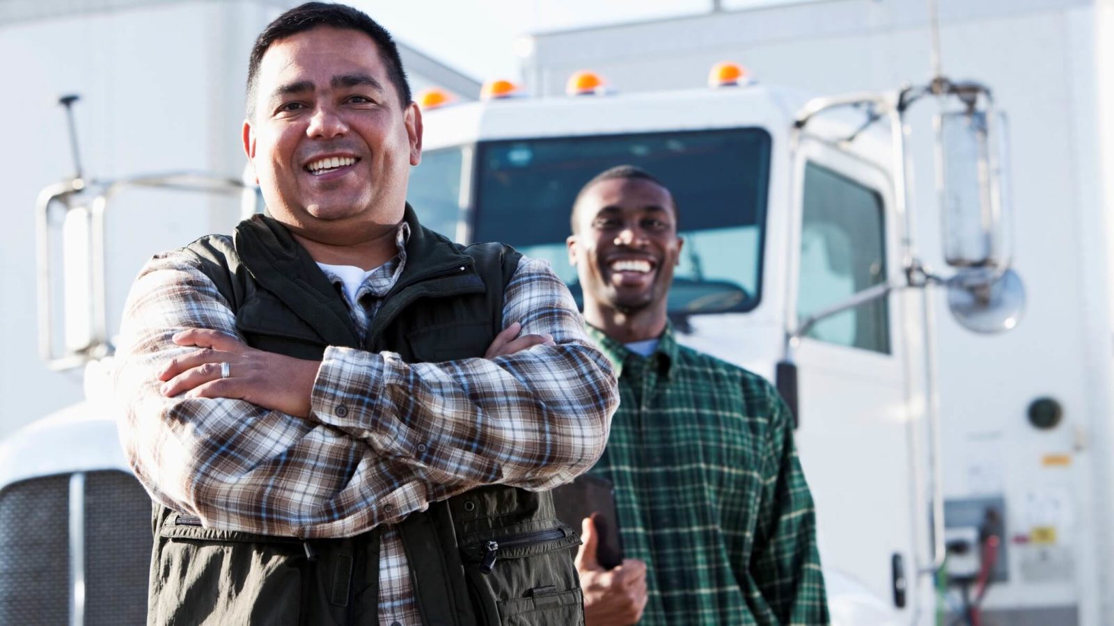Two smiling truck drivers standing in front of white semi-trucks