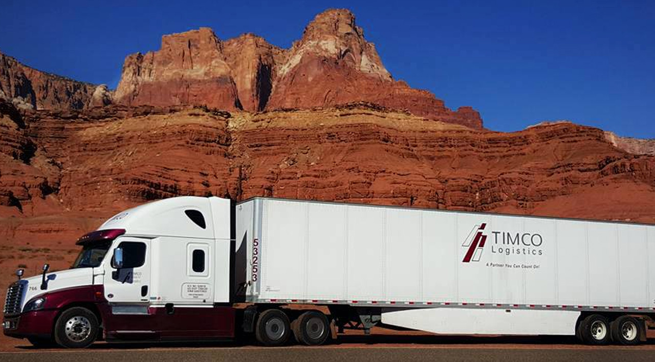 White Timco Logistics semi-truck driving past red rock cliffs