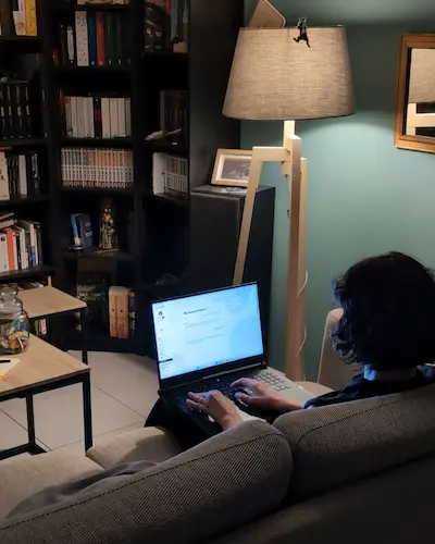 Une femme vue de dos assise sur un canapée et utilisant un ordinateur. 