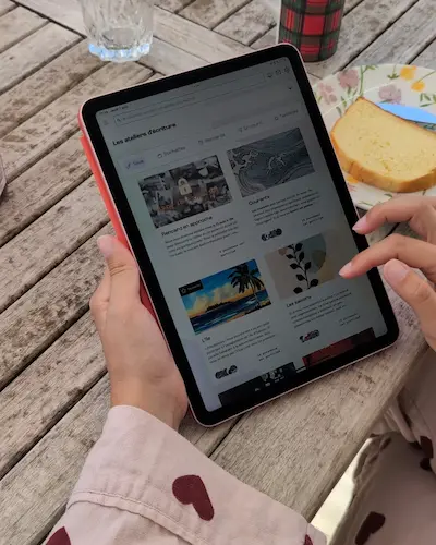 Une personne assise à une table tenant une tablette ouverte sur Pochade la plateforme d'écriture, sur la page des ateliers d'écriture.