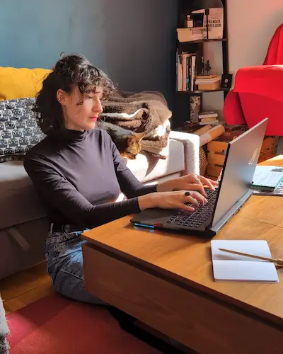Une femme assise près d'un canapé utilisant un ordinateur portable.