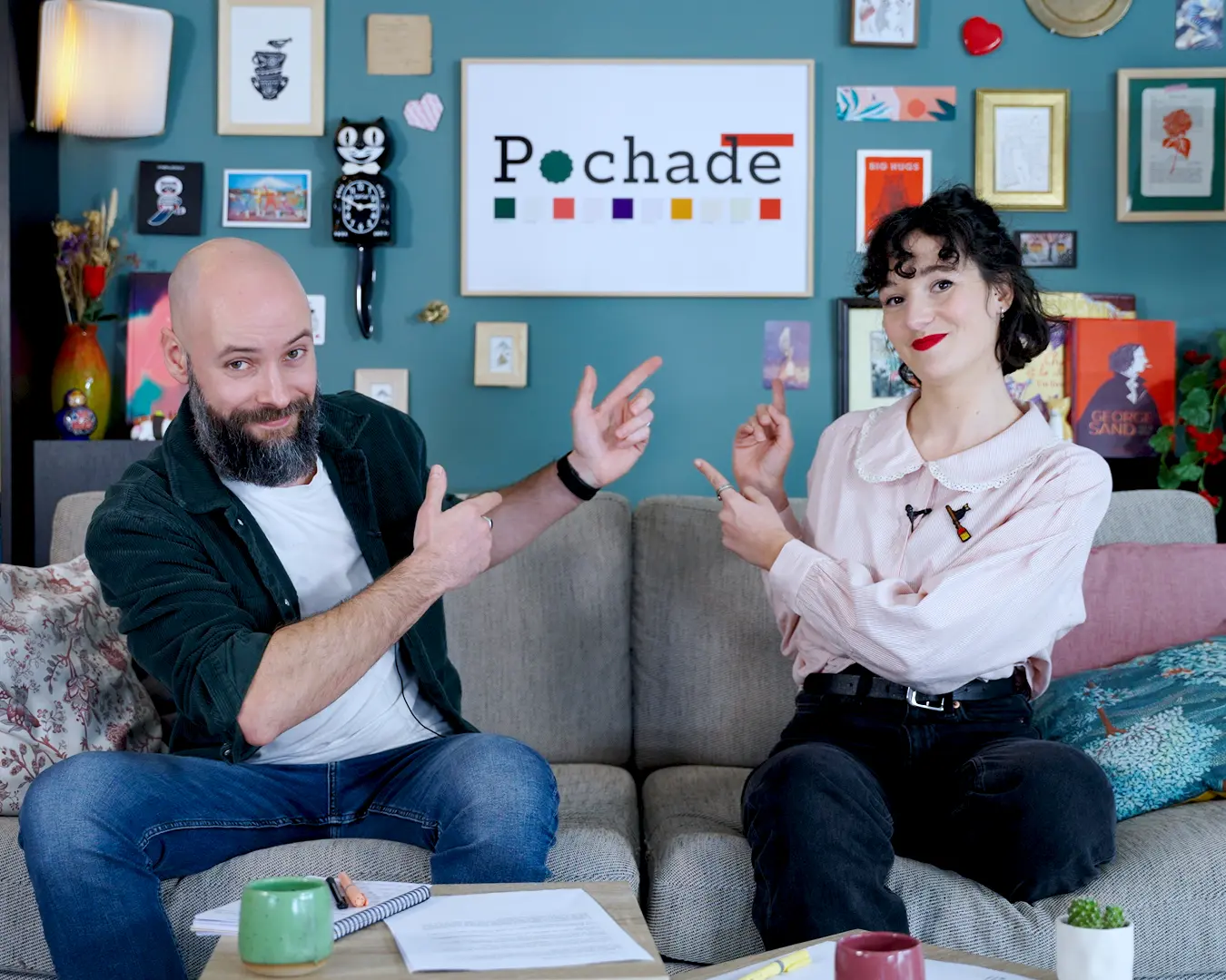 Romain et Fanny, les fondateurs de l'équipe de pochade, assis sur un canapé et montrant le logo de Pochade la plateforme d'écriture. 