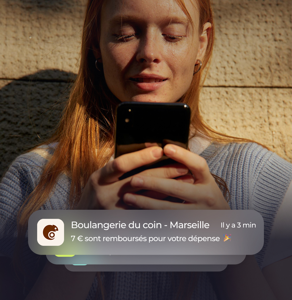 Femme consultant son smartphone recevant une notification de remboursement de 7 € après un achat à la boulangerie du coin à Marseille.