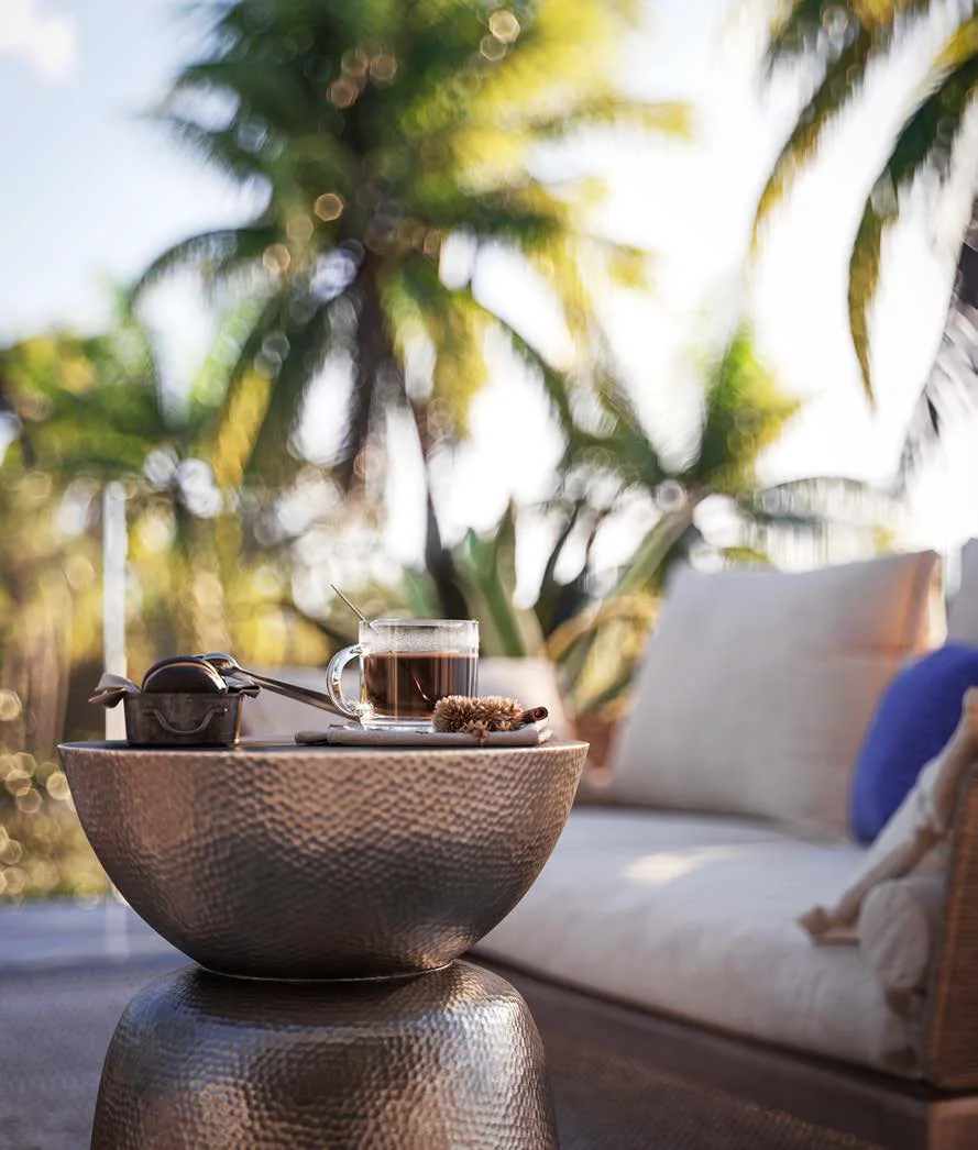 Hammered bronze side table with tea service on a palm-shaded terrace at Four Seasons Nevis Peak Residences