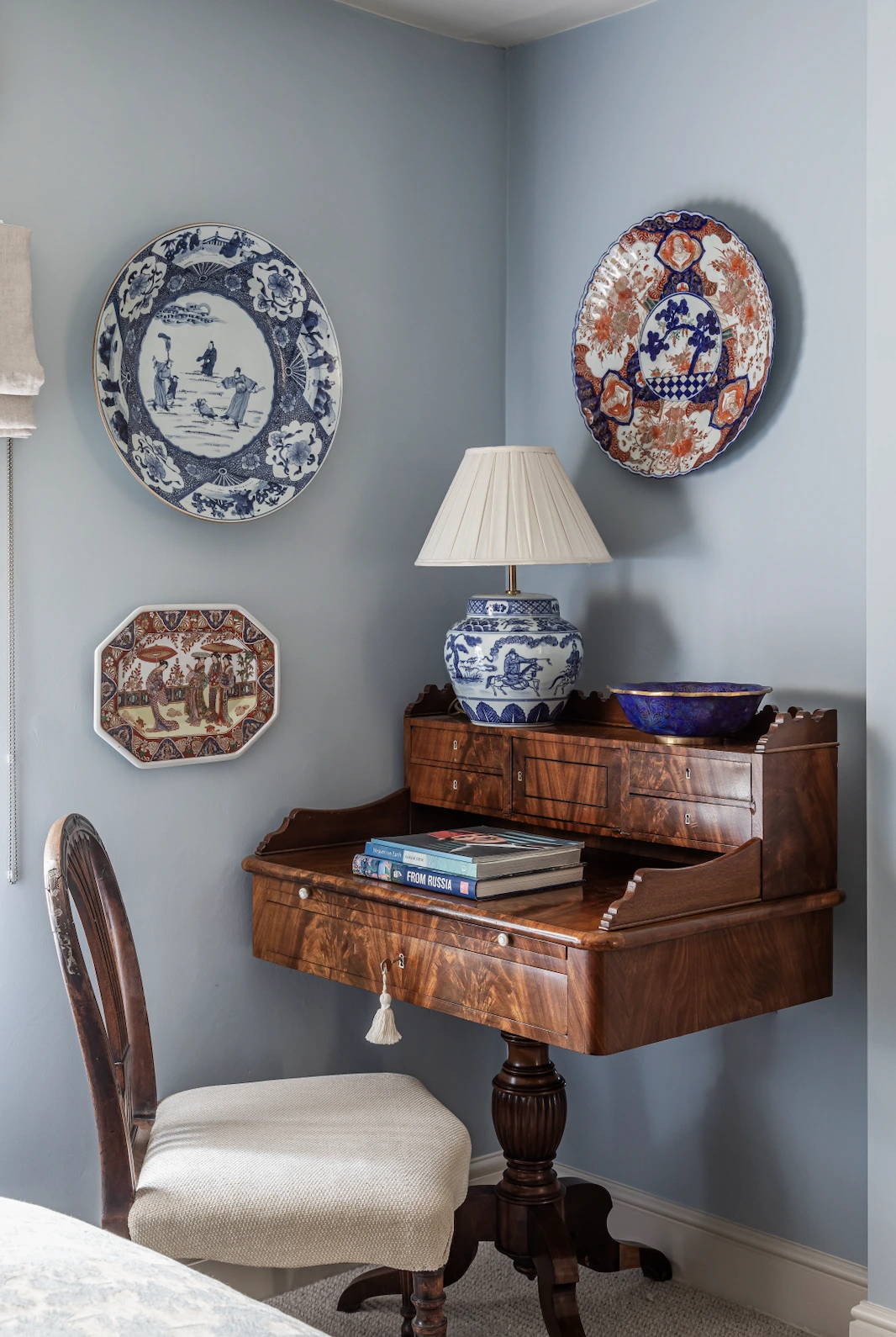 Antique mahogany writing desk with a blue-and-white ginger jar lamp and decorative Imari plates on a pale blue wall at Mabel, Suffolk