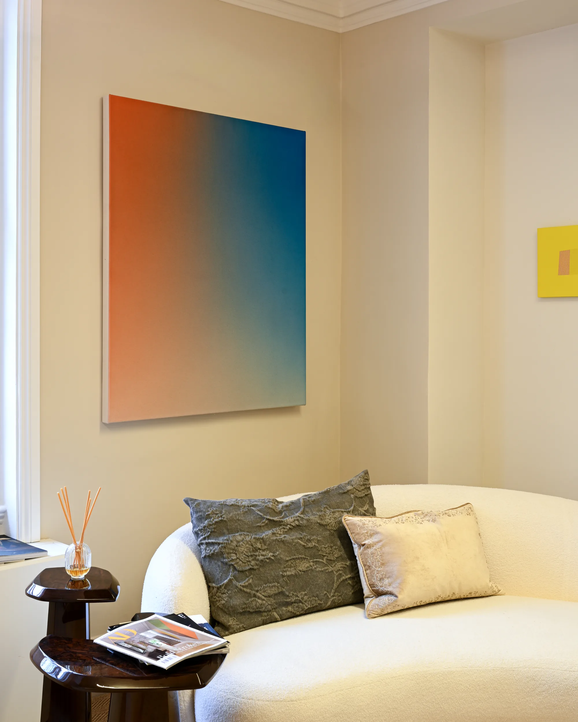 Orange and blue gradient painting above a cream curved sofa