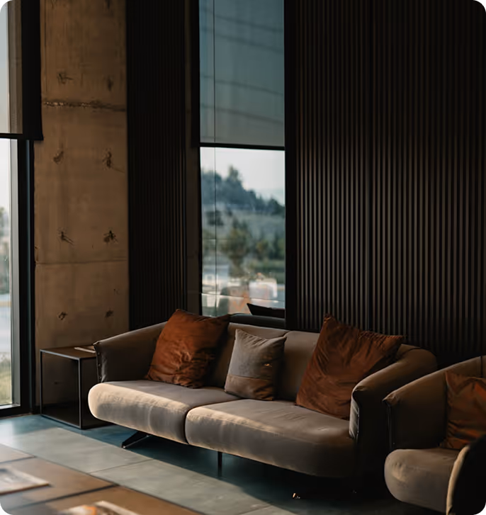 Modern indoor seating area with a beige sofa and two brown pillows, positioned next to a window showing an outdoor view.
