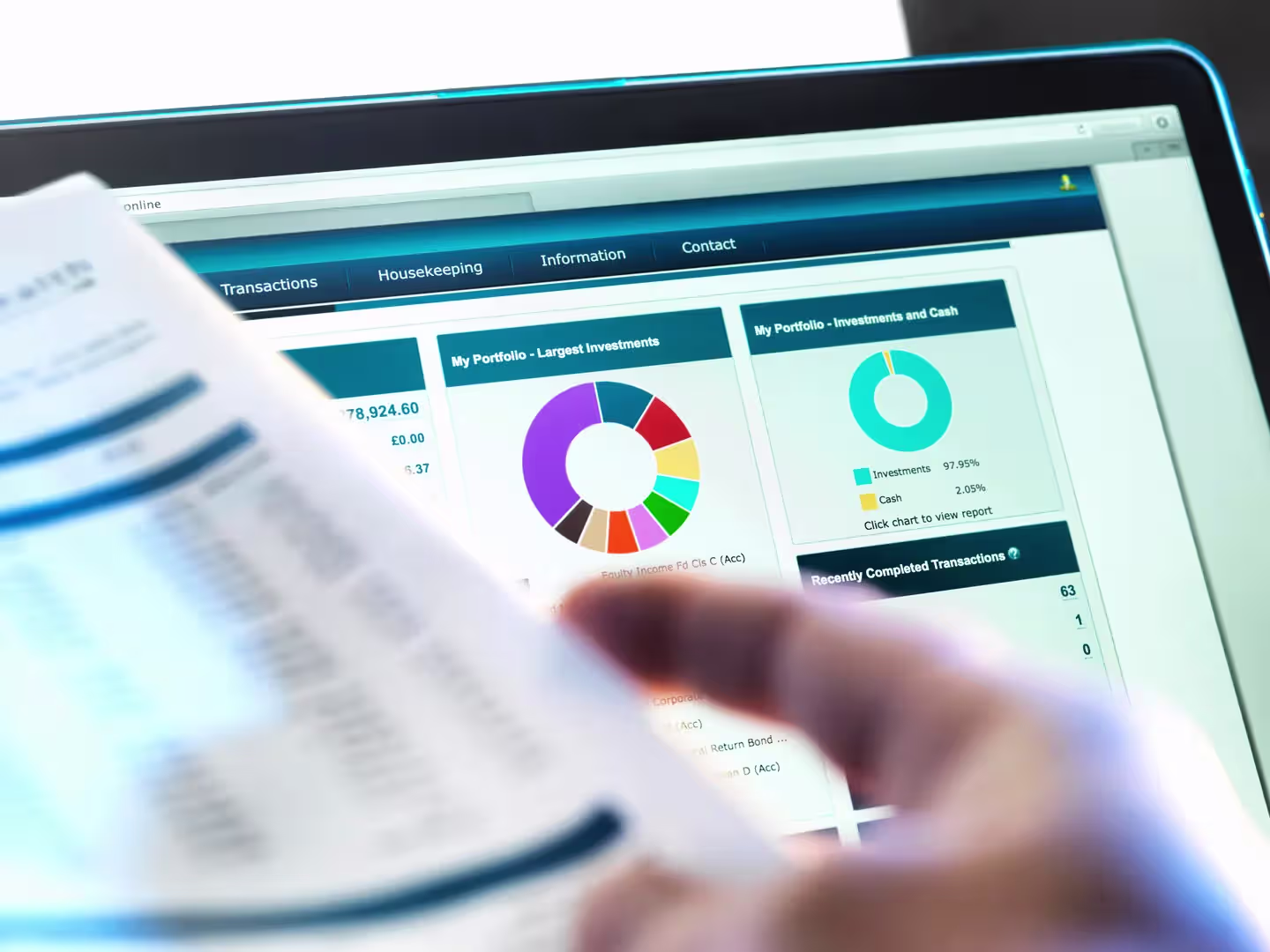 Investor reviewing a portfolio dashboard with allocation charts on a laptop screen while holding a financial statement.