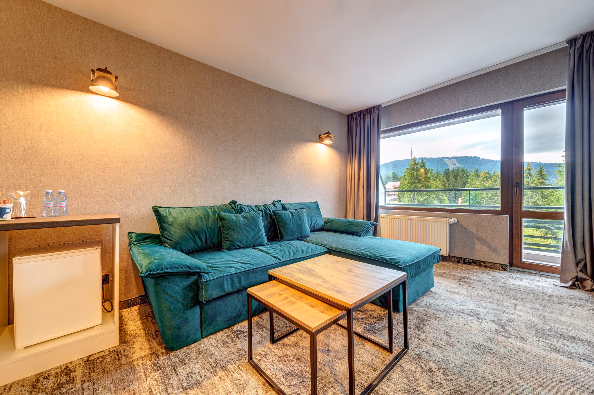 Удобен кът за сядане в апартамент на Гранд Хотел Мургавец с плюшен кафяв диван, червен фотьойл и масичка за кафе, подредена с вино и пресни плодове.