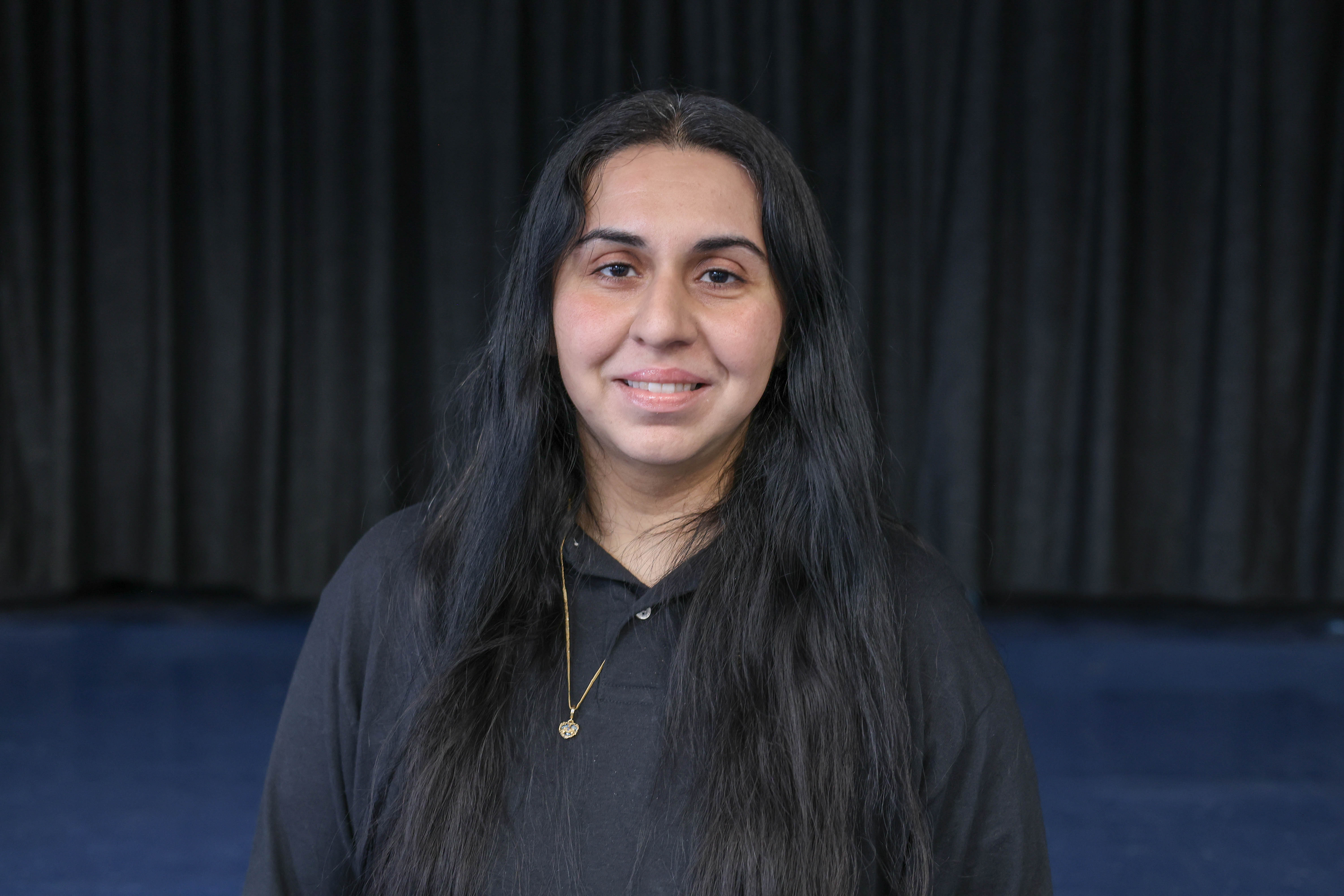 Nishat Fabia smiling in front of a dark curtain backdrop