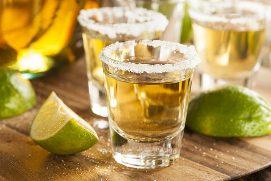 Three tequila shots with salted rims beside lime wedges.