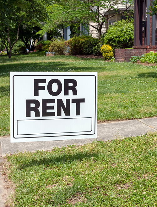 A white "For Rent" sign in the front yard of a house.