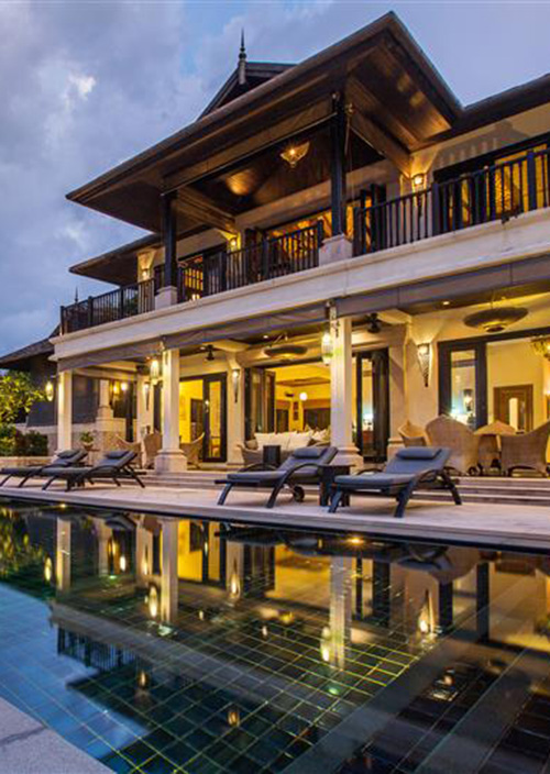A spacious house at night, with bright lights reflecting off a serene pool, creating a tranquil outdoor atmosphere.