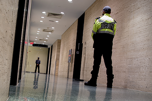Two security guards standing in a polished hallway facing each other in a large building.