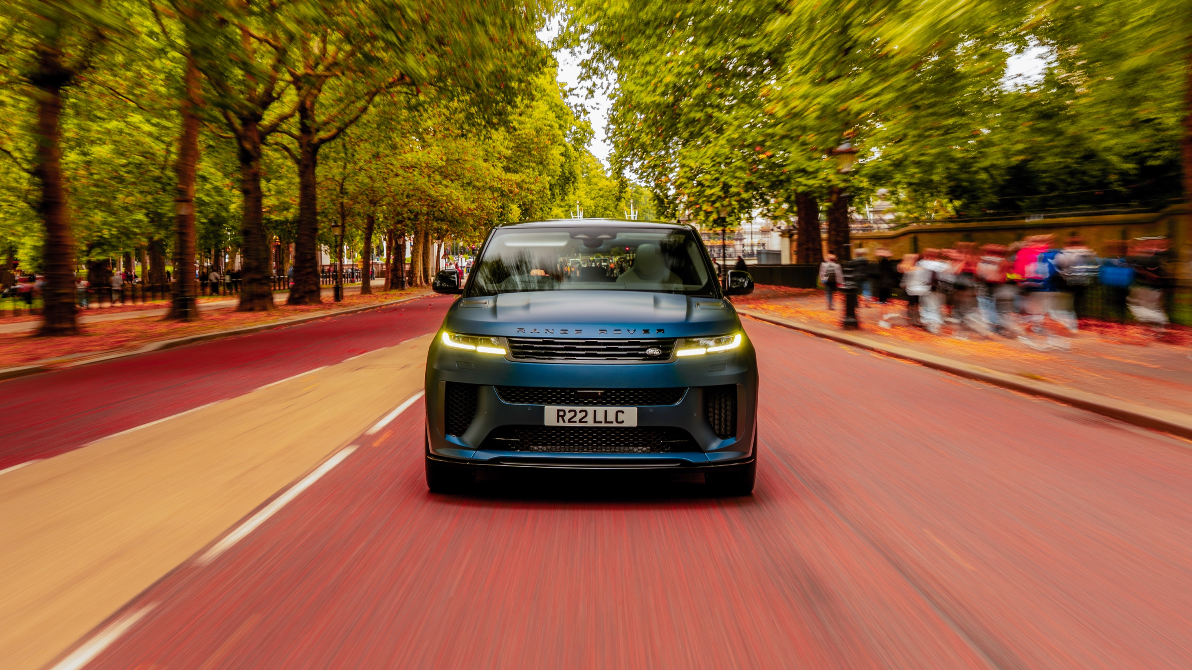 A dynamic action shot of the matte blue Land Rover Sport SV driving through a central London thoroughfare, capturing its power and presence amidst blurred city traffic and classical architecture.
