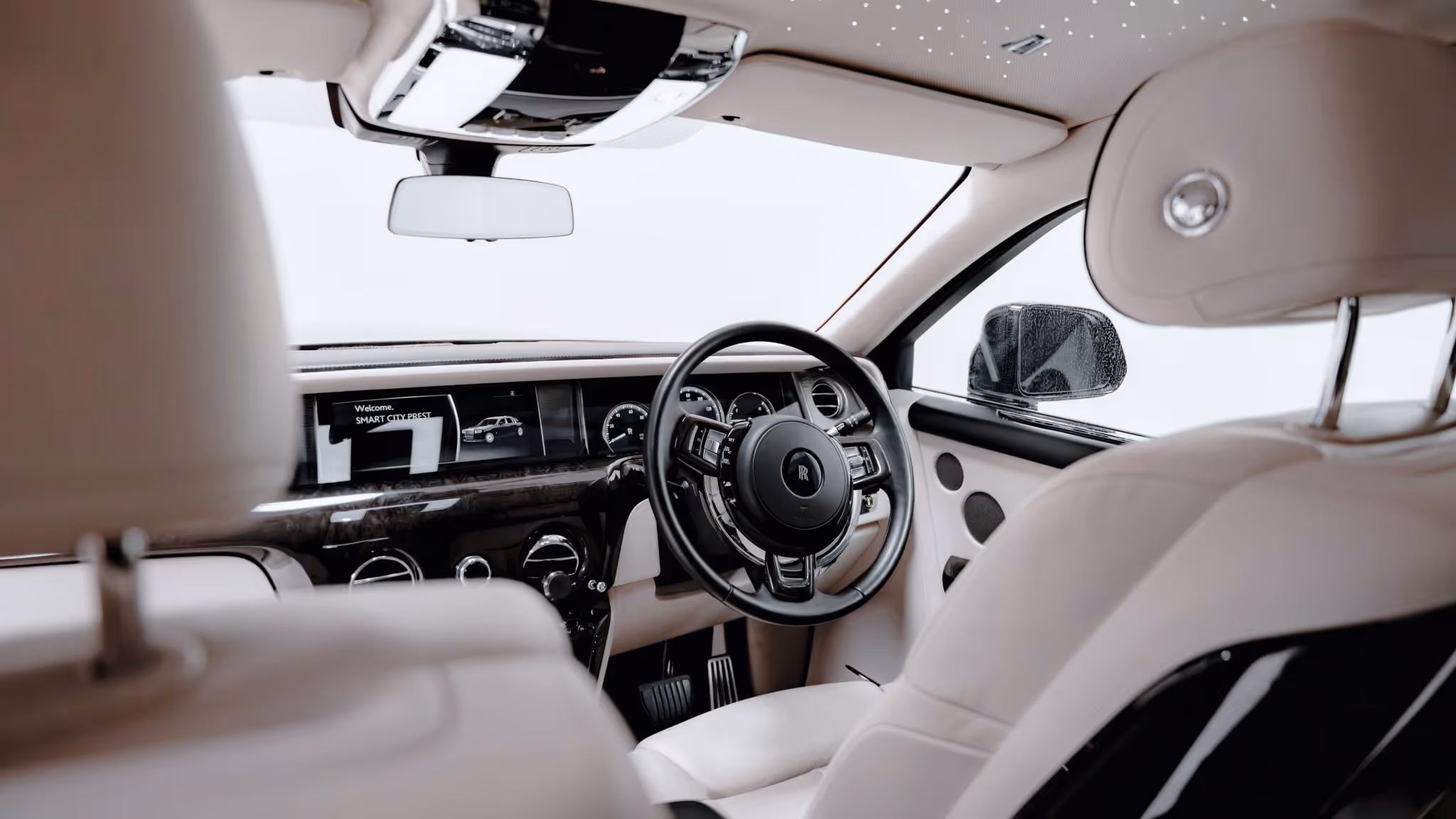 Interior view of a Rolls-Royce Phantom showcasing the luxurious white leather cabin, signature starlight headliner, and elegant dashboard detailing.