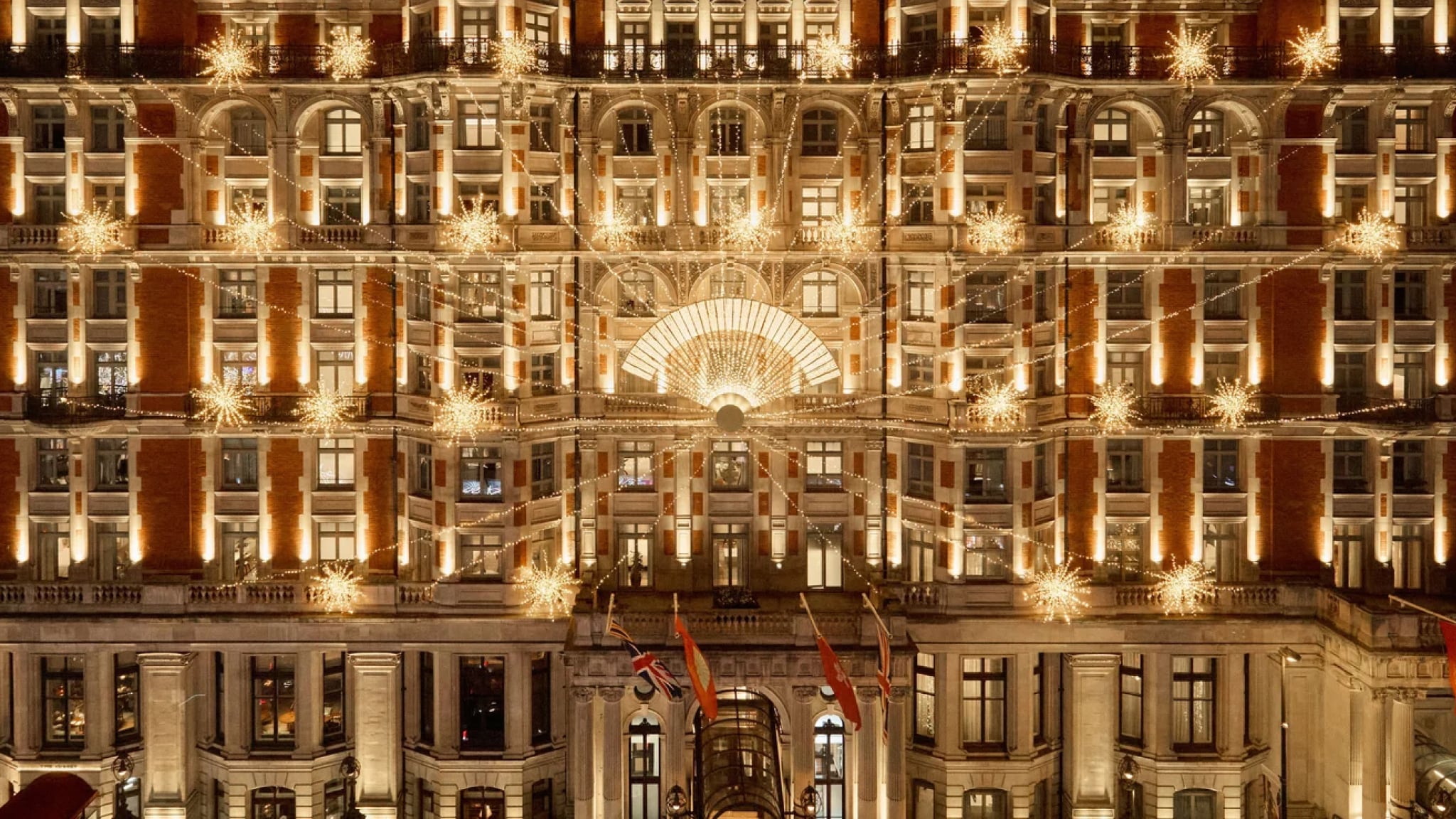 Grand exterior of Mandarin Oriental Hyde Park decorated with elaborate Christmas lights and golden star-shaped ornaments illuminating the entire façade.