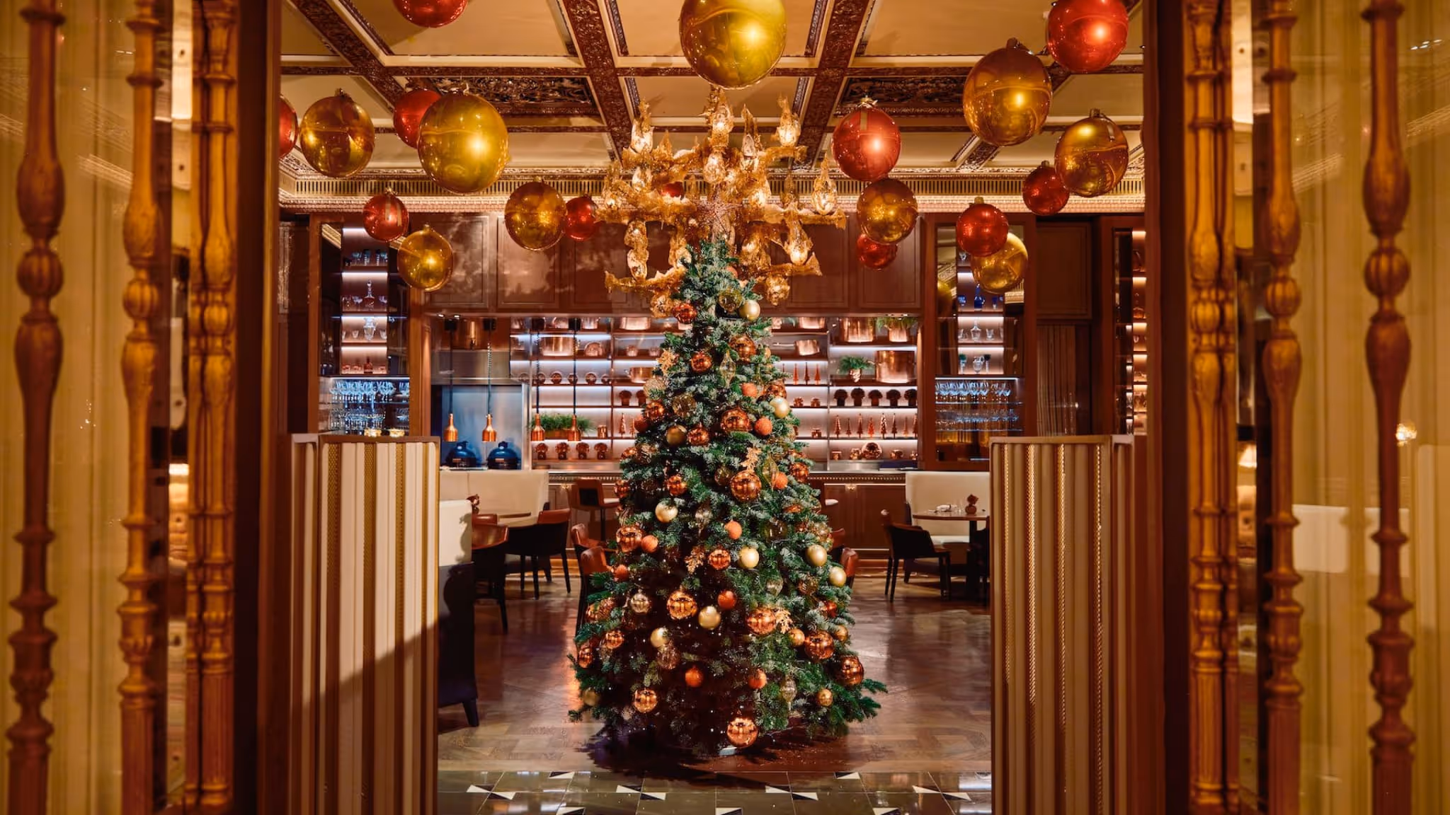  Luxurious Dorchester Promenade at Christmas with gilded pillars and festive trees, set for the legendary afternoon tea.
