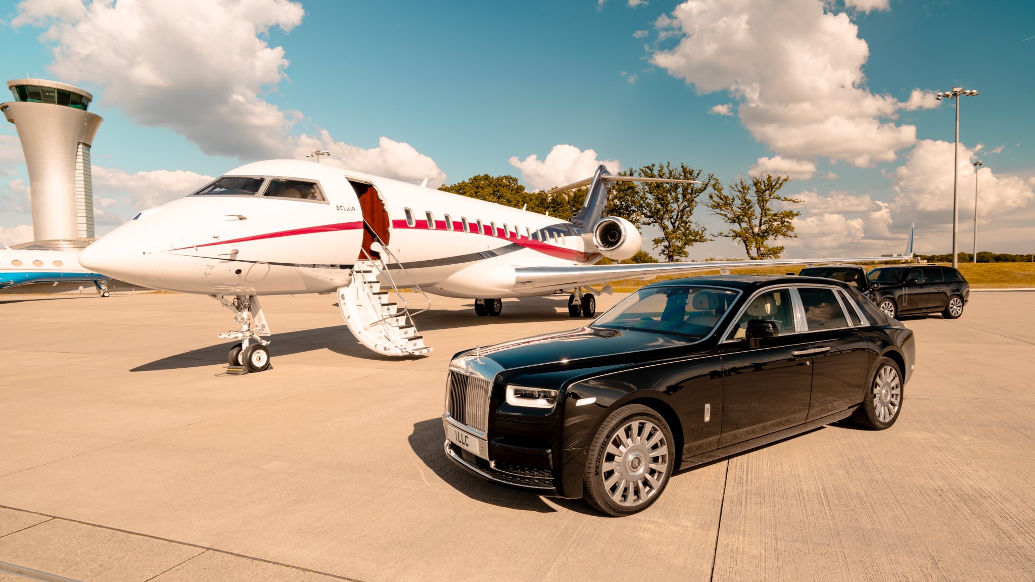 A black Rolls-Royce Phantom parked next to a private jet on an airport runway under a bright, partly cloudy sky.