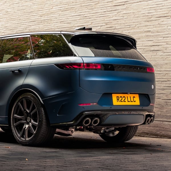 A dynamic rear three-quarter view of a Range Rover Sport SV finished in matte blue, showcasing its bold quad exhausts, sleek LED taillights, and sporty stance against an urban backdrop.