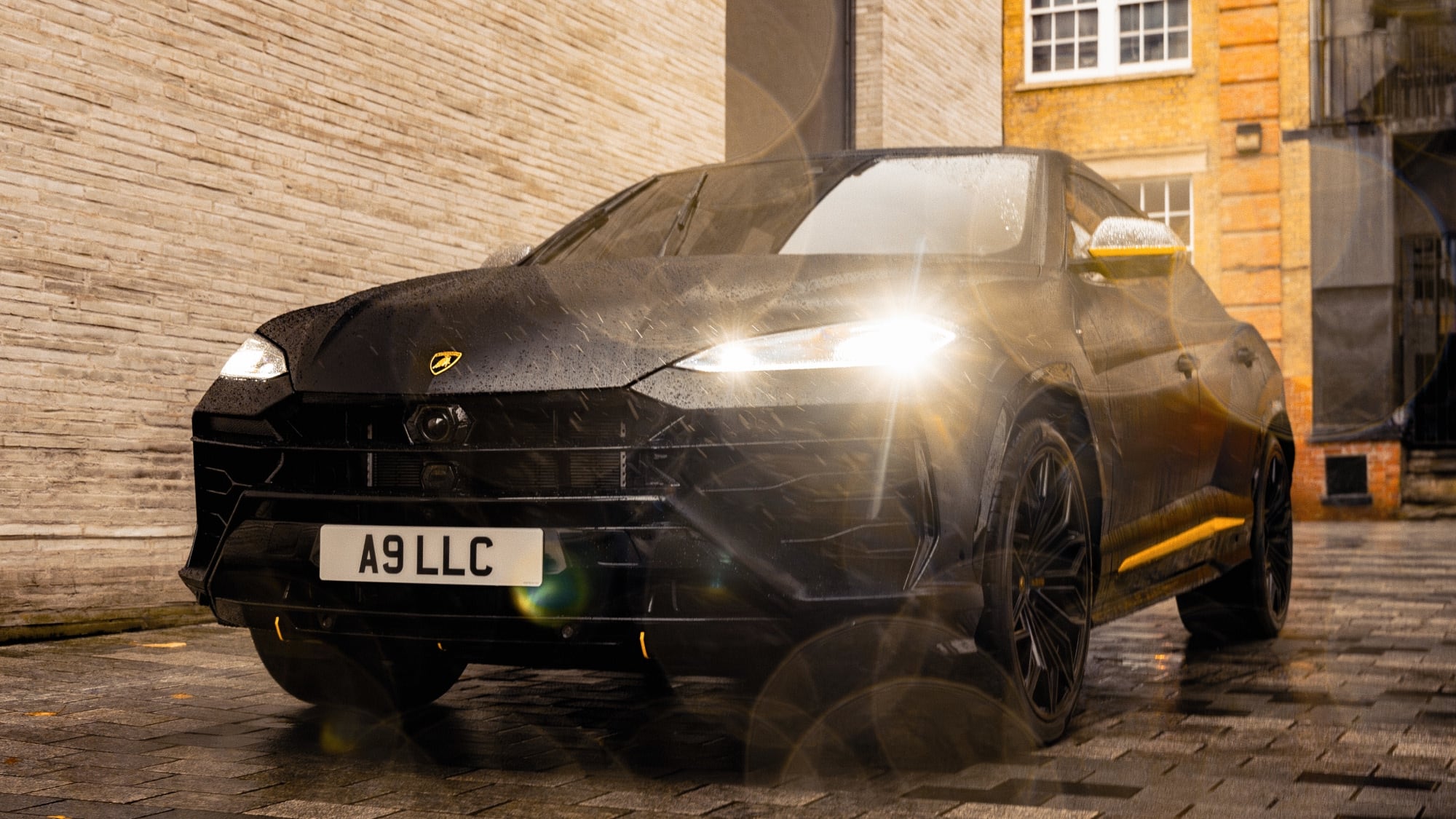 Front view of a Lamborghini Urus parked in rainy conditions with headlights illuminated.