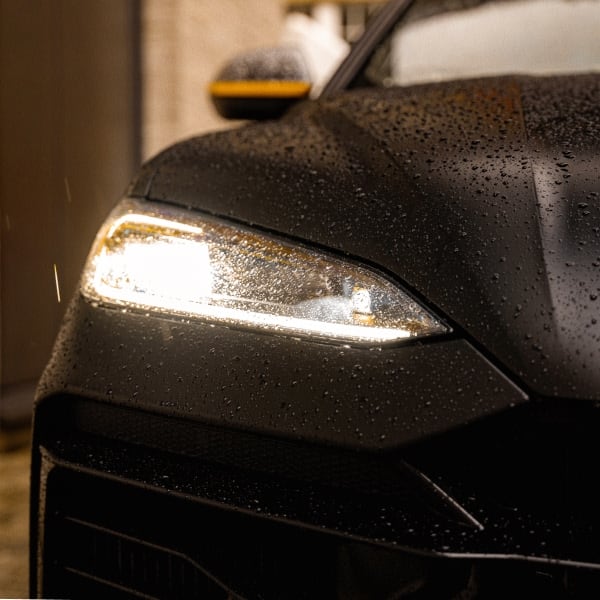 Close-up of a Lamborghini Urus front headlight with rain droplets.
