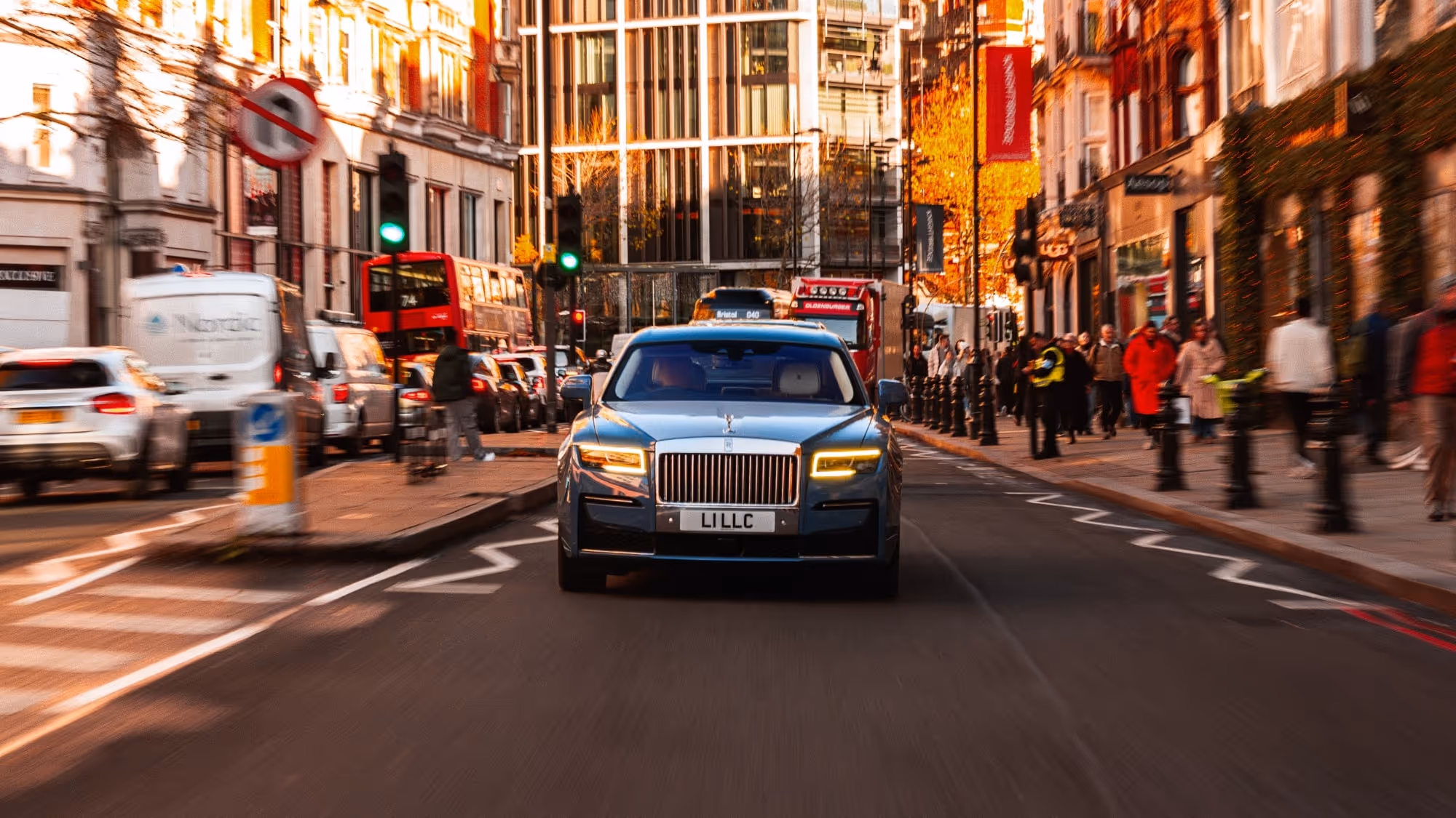 Front view of the Rolls-Royce Ghost navigating a busy central London thoroughfare, utilising motion blur to convey LLC's swift, fluent city mobility.