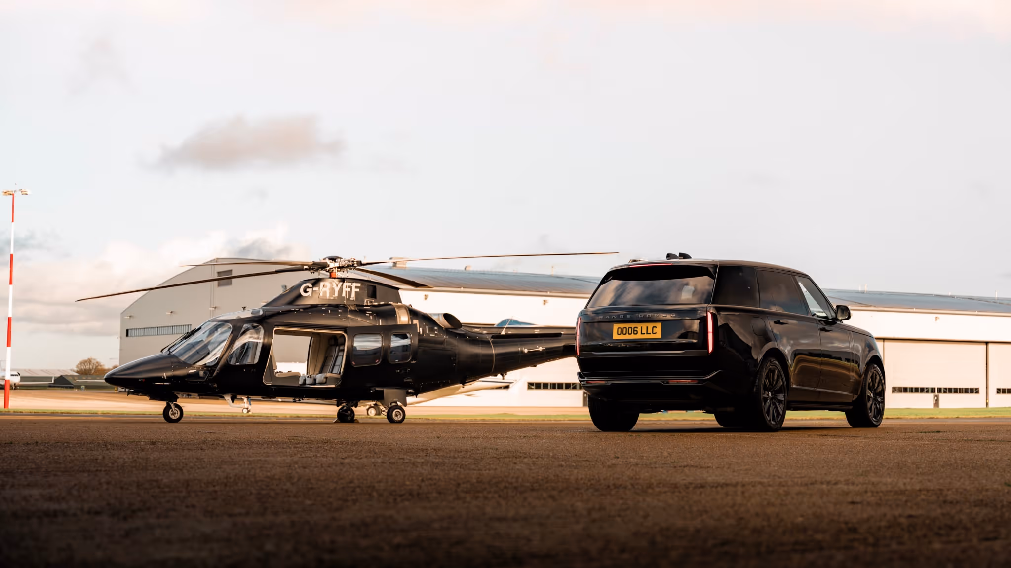 A black Range Rover parked next to a black luxury helicopter on an airfield, representing LLC’s orchestrator role in complex, high-value journeys.
