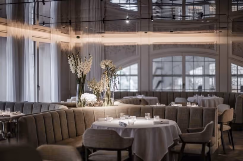 An elegant, softly lit restaurant interior with white-clothed tables and floral arrangements, illustrating the continuity of luxury service regardless of geography.