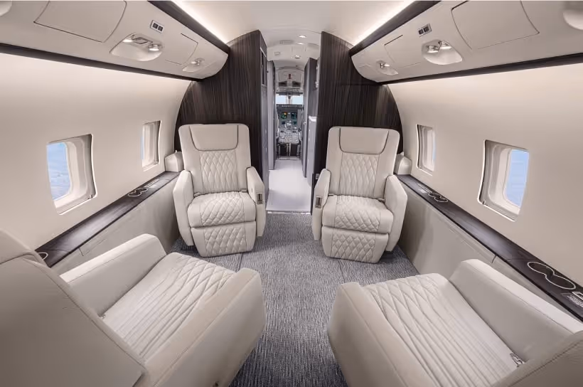 Interior view of a private aircraft featuring four white leather quilted seats and a view toward the cockpit, emphasising efficiency and privacy for intercontinental travel.
