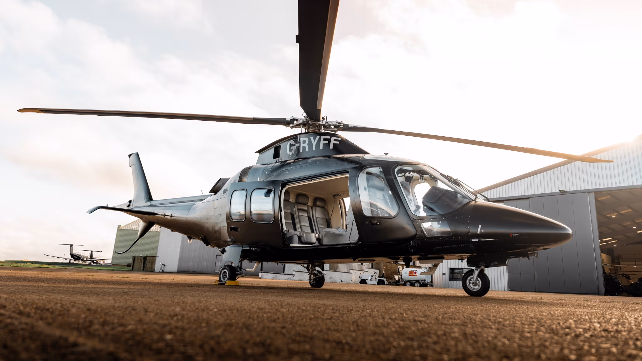 A sleek black Agusta helicopter with the registration G-RYFF parked on a tarmac, used by LLC to bypass congestion and provide operational control for clients.
