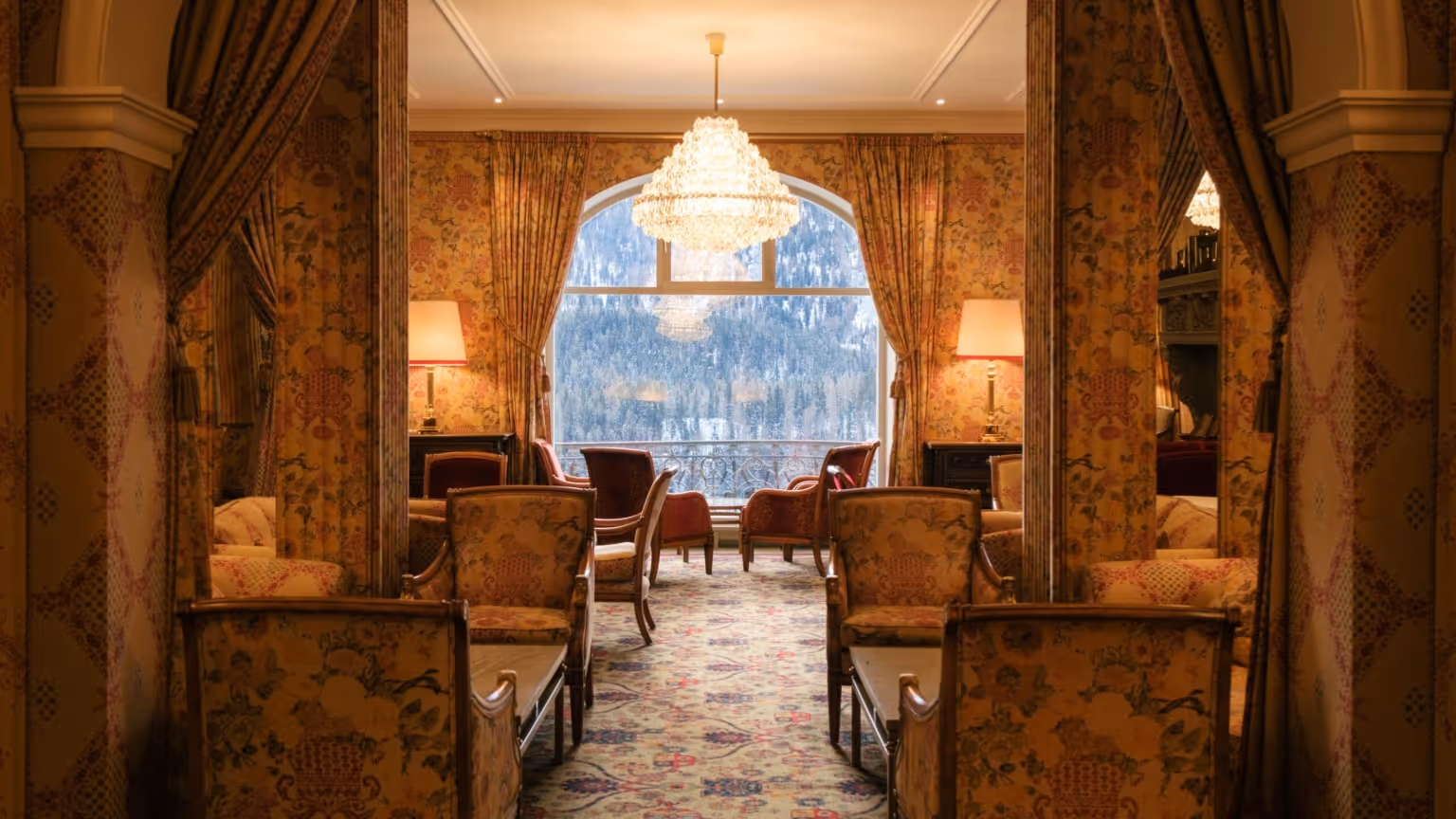 Kulm Hotel lobby in St. Moritz featuring classic alpine interiors, crystal chandelier lighting, patterned textiles, and mountain views through large windows.