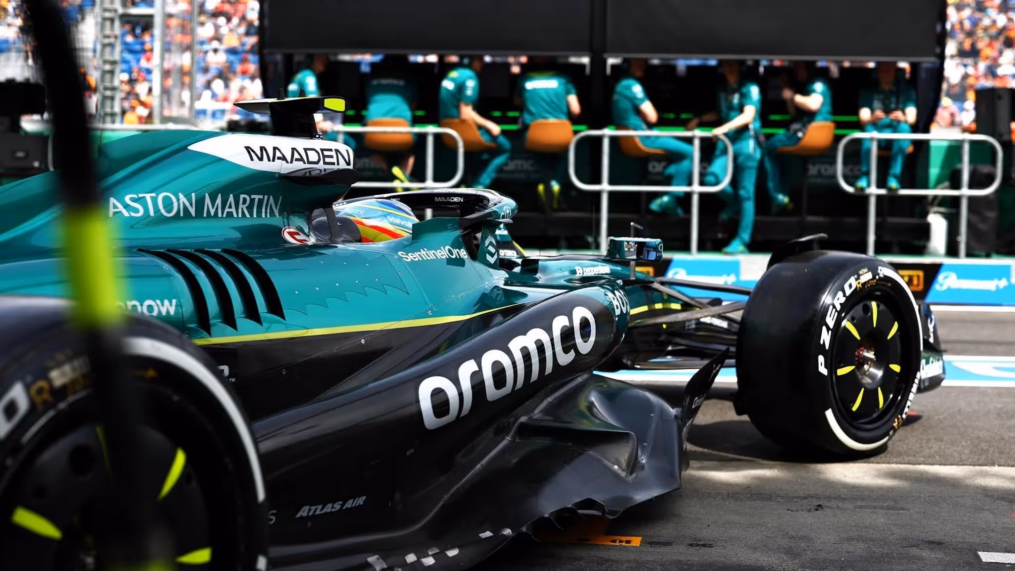A close-up, shallow depth-of-field shot of the emerald green Aston Martin, featuring Aramco branding and the technical crew in the background.