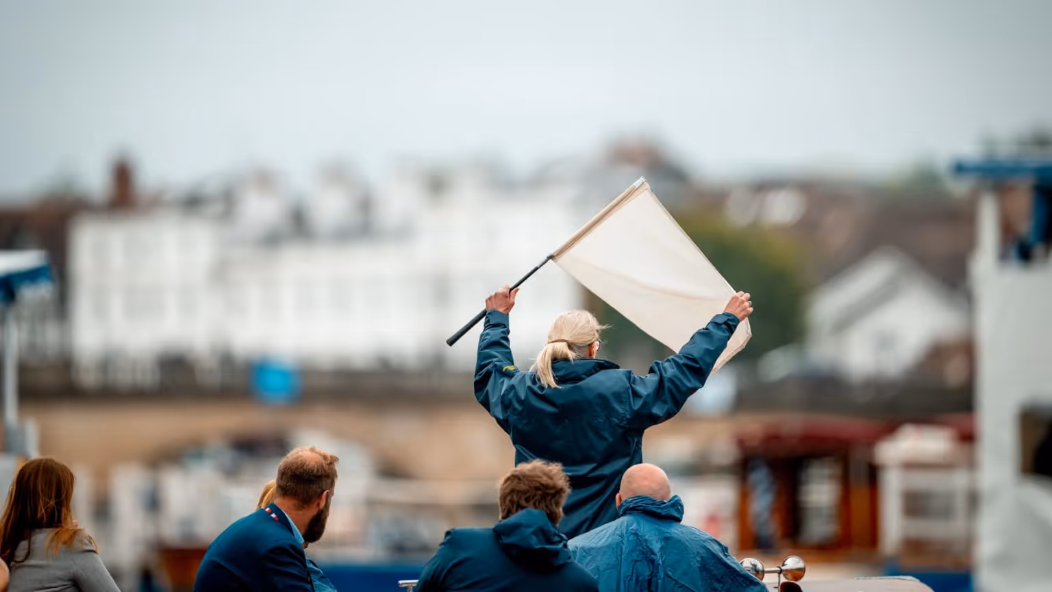 ALT: People seated on a covered boat watching activity along the River Thames with riverside buildings in the background.