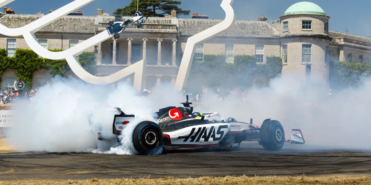 A Formula 1 race car creating smoke during a burnout demonstration at the Goodwood Festival of Speed in front of Goodwood House.