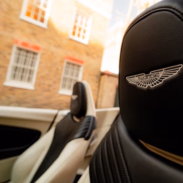 A close-up of the Aston Martin DB11 Volante leather headrest featuring the embroidered Aston Martin wings logo, highlighting the premium craftsmanship and luxury interior detailing.